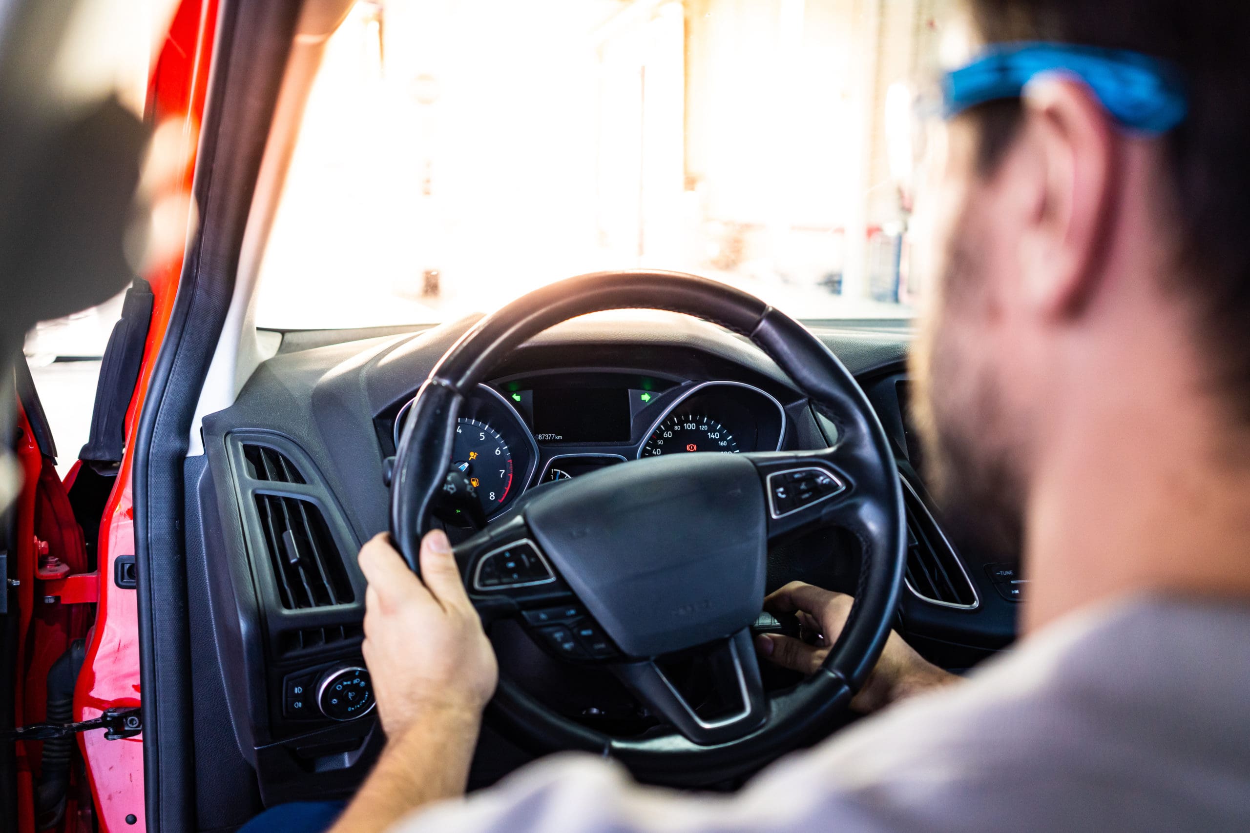 Technician with safety glasses starting the engine of a red car during a vehicle inspection